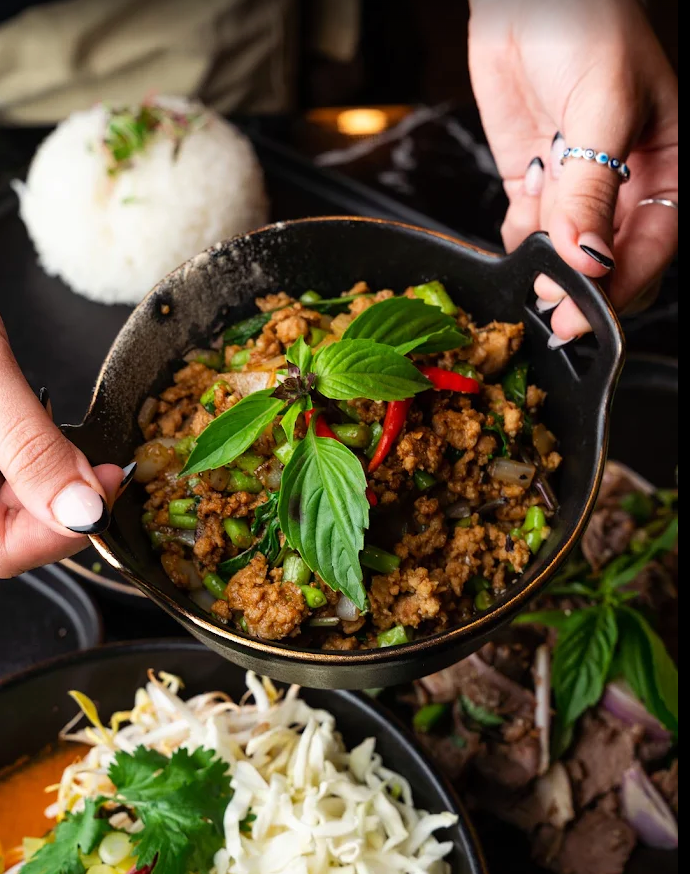 Thai basil stir-fry with fresh basil leaves and red chilies in a black bowl